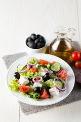 Fresh Greek salad made of cherry tomato, ruccola, arugula, feta, olives, cucumbers, onion and spices. Caesar salad in a white bowl on wooden background. Healthy organic diet food concept.