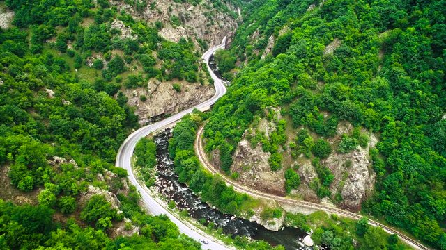Aerial view of drone over mountain road and curves going through forest landscape