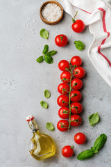 Branch of raw fresh cherry tomatoes, olive oil and leaves basil on gray background. Food background. Selective focus. Top view.