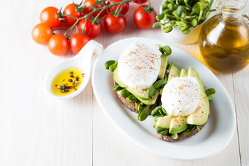 Avocado toast, cherry tomato on wooden background. Breakfast with toast avocado, vegetarian food, healthy diet concept. Healthy sandwich with avocado and poached eggs.