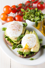 Avocado toast, cherry tomato on wooden background. Breakfast with toast avocado, vegetarian food, healthy diet concept. Healthy sandwich with avocado and poached eggs.