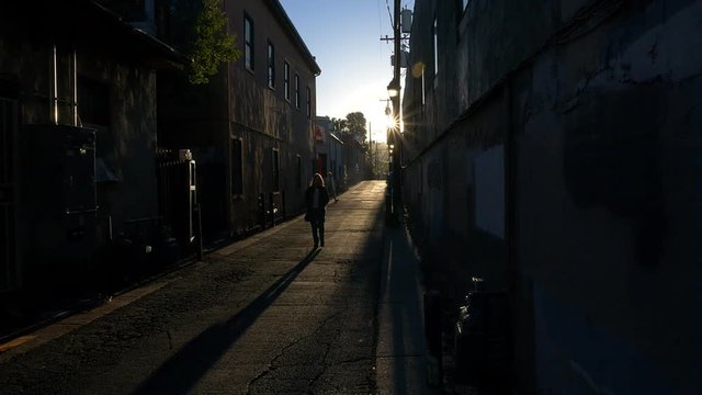 A woman walking in a scary alley, being followed by a man