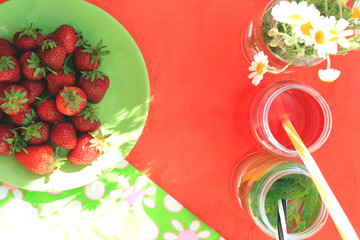 Summer flat lay with bright cocktails,  strawberry and camomile on red and green bright background