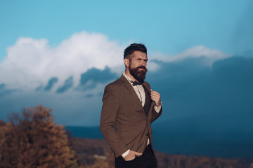 Man in classic coat with bow tie travelling in mountains on summer vacation. Man with beard and...