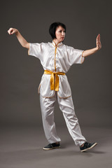 Young woman practicing tai chi chuan. Chinese management skill Qi's energy. Gray background, studio shoot.