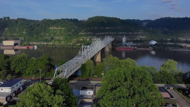 A slow, early morning aerial approach to the Ambridge Bridge spanning the Ohio River. Old factories and coal barges on the shoreline. Pittsburgh suburbs.  	