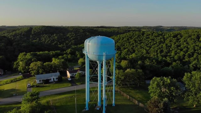 An early evening flyover of a tall water tower in a typical Pennsylvania residential neighborhood. Pittsburgh suburbs.  	