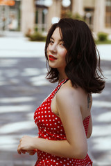 Beautiful woman dressed in a red blouse with polka dots walking down street, looking back.