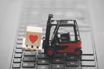 Forklift with red heart symbol on wooden block over laptop keyboard 