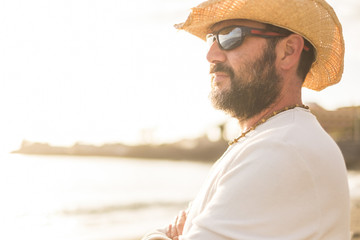 middle age 45 years old caucasian man in vacation look at the horizon with a golde sunset in the background. wearing sunglasses and summer clothes