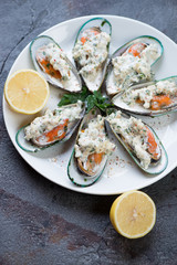 Baked kiwi mussels with cheese sauce and lemon on a white plate, vertical shot, selective focus