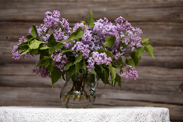 Bouquet of lilac in a glass vase./A bouquet of lilac on a white tablecloth table.
