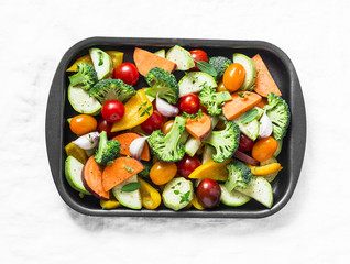 Raw fresh vegetables on a baking sheet. Sweet potato, zucchini, sweet pepper, cherry tomatoes, garlic, broccoli cabbage-ingredients for healthy vegetarian lunch on white background, top view