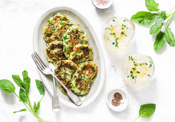 Spinach, zucchini, green peas, garden herbs fritters and white wine on a light background, top...