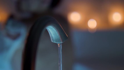 Female Taking a Candlelit Bath Sitting Move Left. a slow motion view of a female taking a bath by candle light, focus on foreground bath faucet and candles