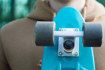 Close-up view of the hipster hands holding his blue plastic penny board in vertical position. The...
