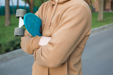 Side view of the young man holding his blue plastic penny board . The concept of modern culture,...