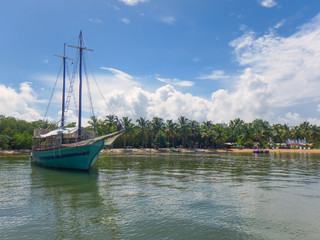 Naklejka na ściany i meble two mast yachts parked in the ocean by the shore, covered with palm trees and tropical plants, against the blue sky and clouds, Punta Cana, Dominican Republic