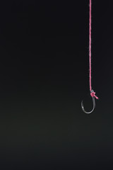 Fototapeta na wymiar Fishing hook tied with red rope hanging on a black background.