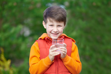 Outdoor portrait of happy Caucasian boy with a glass of water.