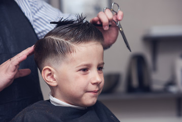Cheerful Caucasian boy  getting hairstyle in barbershop. - obrazy, fototapety, plakaty