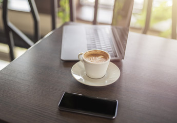 Coffee, smartphone and computer on wooden table in restaurant