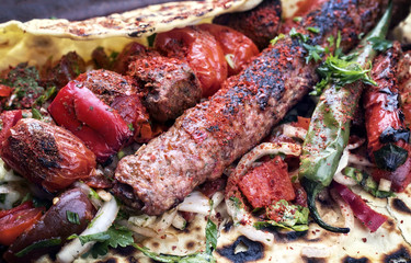 Traditional Adana Kebap with tomato and salad on a flatbread as close up