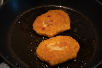 Two breaded schnitzel frying in a pan 