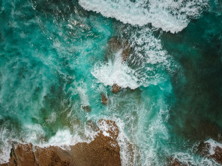 Aerial view of ocean waves and brown rocks in the coastline