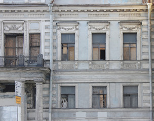Fototapeta premium Old Abandoned Building Facade with Crumbling Pale Grey Aged Walls and Broken Windows. Damaged Residential Apartment House in Need of Renovation and Construction, Bad Living Conditions Concept.