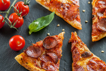 delicious fresh cooked slices of pepperoni pizza on slate with cherry tomatoes red pepper and basil leafs