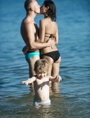 Child with kissing father and mother. Family travel with kid on mothers or fathers day. Summer vacation of happy family. Love and trust as family values. Mother and father with son in sea on beach.