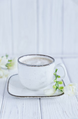 White cup of coffee cappuccino and white freesia flower on white wooden background. Free space, vertical photo