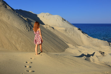 Dziewczyna spaceruje po piaszczystej wydmie, brzegiem morza.