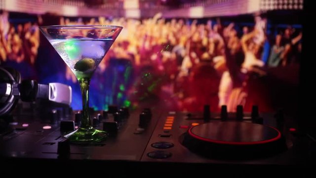 Glass with martini with olive inside on dj controller at nightclub. Dj Console with club drink at music party in nightclub with disco lights.