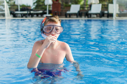 Teenager boy wearing mask swimming in the pool. Happy holiday concept. Cute happy little boy swimming and snorking in the swimming pool.