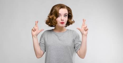 Charming young girl in a gray T-shirt on a gray background. The girl crossed her fingers in her arms
