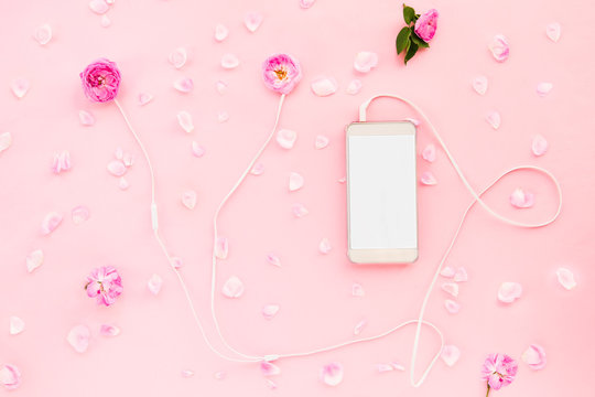 Romantic fashion layout - top view white headphones with pink rose flowers, smartphone and rose petals on the pink background. Relax and delicate sound, music concept. Selective focus, space for text.