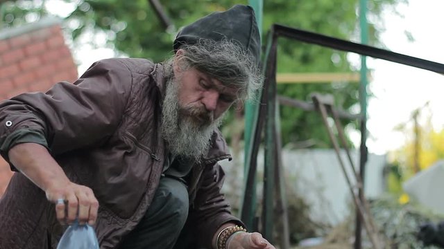 A homeless old man is washing and drinking water in a dump
