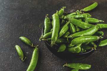 Raw fresh green pea in black bowl, dark rusty background copy space