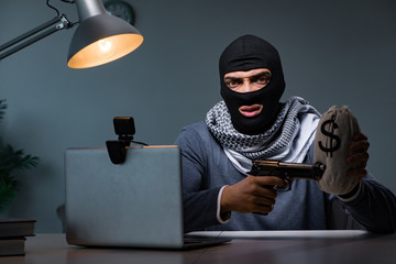 Terrorist burglar with gun working at computer