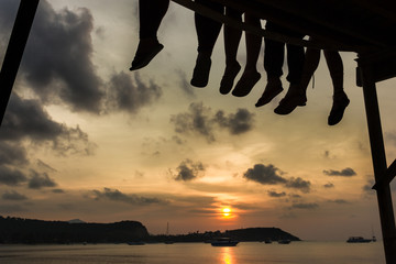 Group of friends enjoying a warm sunset while sitting on the dock of the bay in the island of Koh...