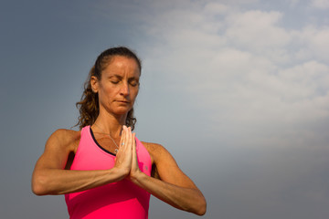 Woman meditating with hands together on the beach in Goa with blue sky on the background. Peaceful, focus, zen-like moment concept