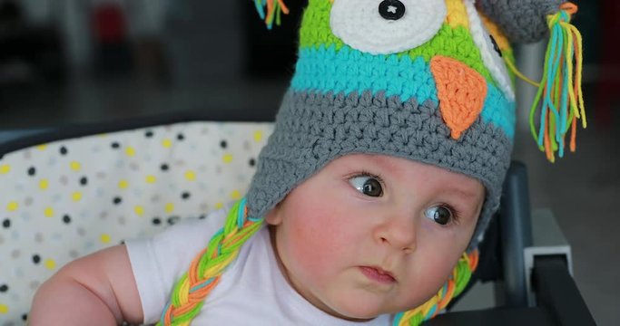Beautiful Baby With A Funny Colored Wool Hat On The Head, Cute Six Month Old Baby Boy In High Chair. Close Up View - 4K Resolution

