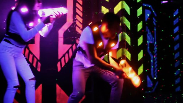 Modern young people with laser pistols playing laser tag on dark labyrinth