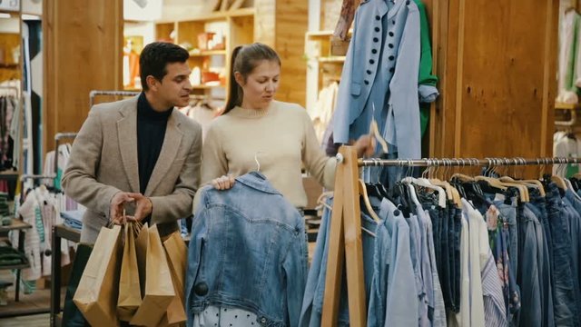 Couple is choosing jeans shirt for her in the clothes store.