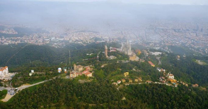 Flying around Tibidabo mountain with amusement park overlooking city of Barcelona, Spain. Aerial helicopter view