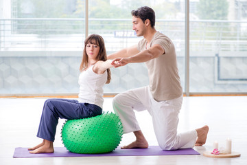 Personal coach helping woman in gym with stability ball