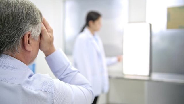 Senior man reading out number from eye chart with one eye close. Old chinese man reading out eye chart with help from young female chinese nurse. Medical concept. Slider dolly shot.