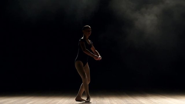 Silhouette of girl ballerina on stage in darkness, slow motion. A little girl is studying ballet on stage in a choreographic school.